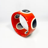 Flat surfaced resin cuff bracelet cast in a 60s inspired abstract pattern of orange, black and white resin. One edge is inlaid with black and white polka dots.