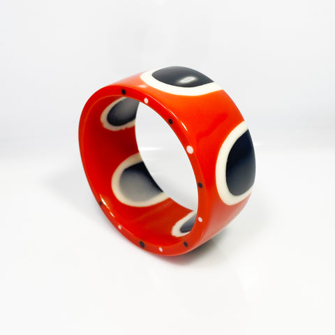 Flat surfaced resin cuff bracelet cast in a 60s inspired abstract pattern of orange, black and white resin. One edge is inlaid with black and white polka dots.
