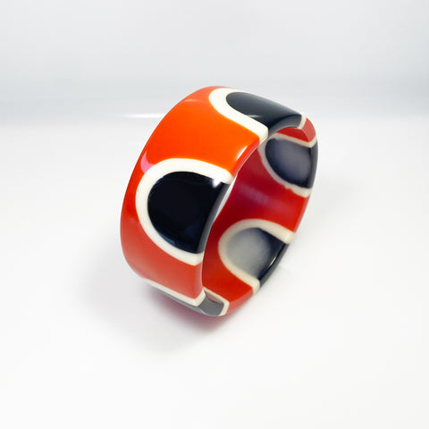 Flat surfaced resin cuff bracelet cast in a 60s inspired abstract pattern of orange, black and white resin. One edge is inlaid with black and white polka dots.