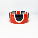 Flat surfaced resin cuff bracelet cast in a 60s inspired abstract pattern of orange, black and white resin. One edge is inlaid with black and white polka dots.