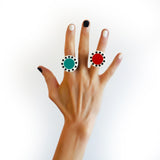 2 of the statement abstract resin rings worn on model's hand. One is inlaid with a teal blue centre, the other displays a orange red centre.