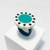 Large circular statement ring handmade from resin. The top is a circle cast in white resin with a teal blue centre, which is surrounded with black polka dots. It is fitted to a black resin blank. 