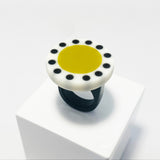 Large circular statement ring handmade from resin. The top is a circle cast in white resin with a lime green centre, which is surrounded with black polka dots. It is fitted to a black resin blank. 