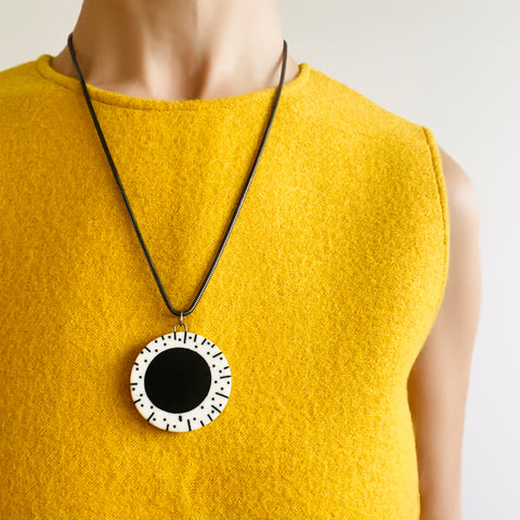 monochrome resin circular pendant, hung on a silver snake chain, worn by model on a yellow top