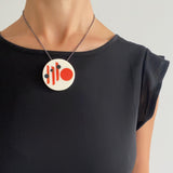 Large circular white resin pendant cast in a Midcentury Modern design of orange stripes and black polka dots. Hung on oxidised silver chain. Worn by model.