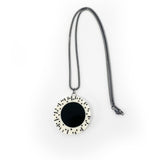 black and white resin circular pendant hung on oxidised silver chunky snake chain. The round pendant is cast in white resin and inlaid with a large black centre. The white edge is decorated with black lines and polka dots.