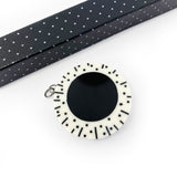 black and white resin circular pendant, by itself, without silver snake chain. The round pendant is cast in white resin and inlaid with a large black centre. The white edge is decorated with black lines and polka dots.