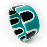 The abstract pop cuff standing upright, displaying its sixties-inspired pattern. Cast in black, white and teal blue resin.