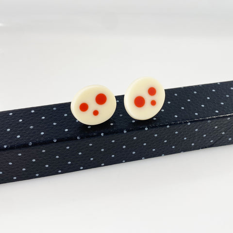 Oval shaped resin sud earrings cast in white and inlaid with orange polka dots. Fitted wit silver pins and disc plastic backs.