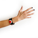 Abstract Pop cuff worn on model's arm. It is a flat surfaced large cuff bracelet, inlaid with a sixties-inspired pattern in black, white and orange resin.