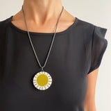Large circle resin pendant cast with a mustard centre and a white border, which is inlaid with black stripes. Hung on oxidised silver chunky snake chain. Worn on model.