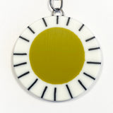 Large circle resin pendant cast with a mustard green centre and a white border, which is inlaid with black stripes.