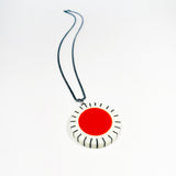 Large circle resin pendant cast with a orange centre and a white border, which is inlaid with black stripes. Hung on oxidised silver chunky snake chain.