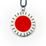Large circle resin pendant cast with a orange centre and a white border, which is inlaid with black stripes. Hung on oxidised silver chunky snake chain.