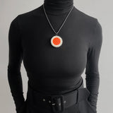 Large circle resin pendant modelled. It is cast with an orange centre and a white border, which is inlaid with black stripes. Hung on oxidised silver chunky snake chain.