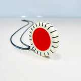 Large circle resin pendant cast with an orange centre and a white border, which is inlaid with black stripes. Hung on oxidised silver chunky snake chain.