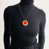 Large circle resin pendant modelled. It is cast with an orange centre and a white border, which is inlaid with black stripes. Hung on oxidised silver chunky snake chain.