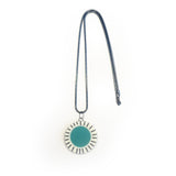 Large circle resin pendant cast with a teal blue centre and a white border, which is inlaid with black stripes. Hung on oxidised silver chunky snake chain.