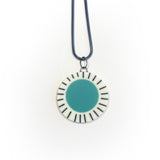 Large circle resin pendant cast with a teal blue centre and a white border, which is inlaid with black stripes. Hung on oxidised silver chunky snake chain.
