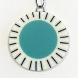 Large circle resin pendant cast with a teal blue centre and a white border, which is inlaid with black stripes.