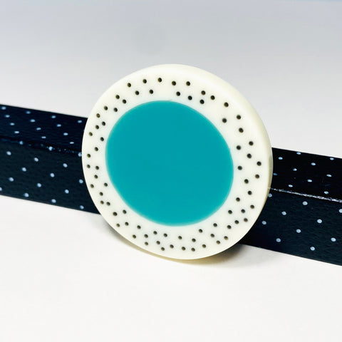 Oversized disc resin brooch with a teal middle and a white border, which is inlaid with black polka dots. Fitted with a surgical steel back.