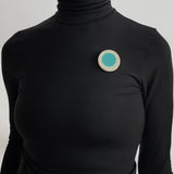 Oversized disc resin brooch with a teal middle and a white border, which is inlaid with black polka dots. Worn by model.