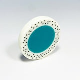 Oversized disc resin brooch with a teal middle and a white border, which is inlaid with black polka dots. Fitted with a surgical steel back.