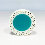 Oversized disc resin brooch with a teal middle and a white border, which is inlaid with black polka dots. Fitted with a surgical steel back.