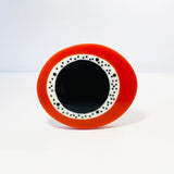 oversized sculptural oval brooch cast in black, white and orange resin, inlaid with black dots.