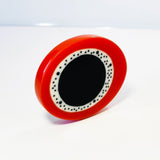 oversized sculptural oval brooch cast in black, white and orange resin, inlaid with black dots.