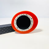 oversized sculptural oval brooch cast in black, white and orange resin, inlaid with black dots.