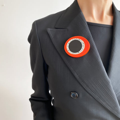 oversized sculptural oval brooch cast in black, white and orange resin, inlaid with black dots. Worn by model.