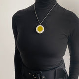 Oversized disc pendant modelled. It is cast in olive green and white resin, and inlaid with black polka dots. Hung on a chunky 20" oxidised silver chain.