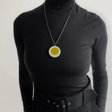 Oversized disc pendant modelled. It is cast in olive green and white resin, and inlaid with black polka dots. Hung on a chunky 24" oxidised silver chain.
