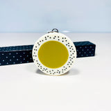 Oversized disc pendant cast in olive green and white resin, and inlaid with black polka dots.