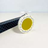 Oversized disc pendant cast in olive green and white resin, and inlaid with black polka dots.