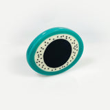 Sculptural oval shaped statement brooch cast in teal, white and black resin, inlaid with black dots.