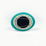 Back of the sculptural teal resin brooch, displaying the pin, handmade from sturdy surgical steel.