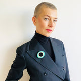 Sculptural oval shaped statement brooch cast in teal, white and black resin, inlaid with black dots. Worn on jacket lapel by model.