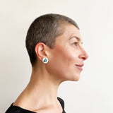 Teal and blue stud earrings, ornate with black polka dots, worn by model.