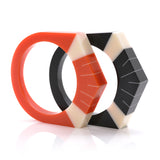 2 Art Deco resin bracelets standing, one orange, one black. Both are inlaid with Deco motif in ivory white.
