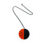 Handmade modernist pendant cast in deep orange red resin, inlaid with black. Hangs on oxidised silver chain.