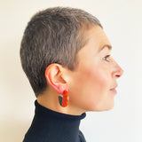 Model wearing Lunula disc hoop earrings, handmade from orange and black resin.