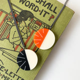 2 modernist Lunula resin necklaces, one orange and white, the other black and white. Both are displayed on a vintage book.