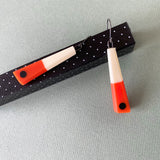 Minimalist chopstick shaped earrings cast in orange and white resin, inlaid with a black dot. Fitted with oxidised silver hooks.