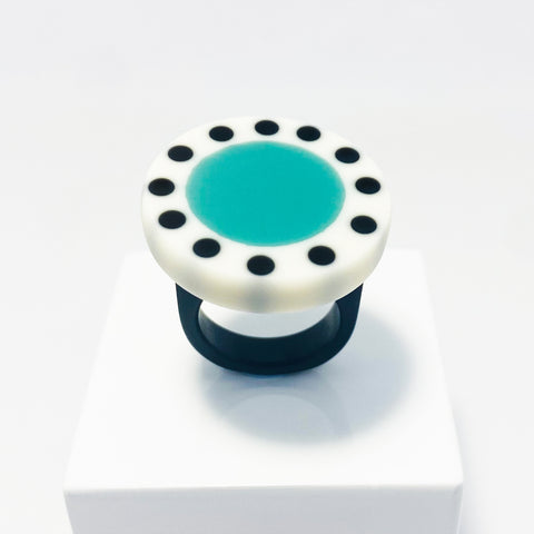 Large circular statement ring handmade from resin. The top is a circle cast in white resin with a teal blue centre, which is surrounded with black polka dots. It is fitted to a black resin blank. 