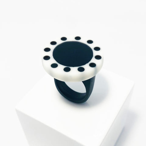Large circular statement ring handmade from resin. The top is a circle cast in white resin with a black centre, which is surrounded with black polka dots. It is fitted to a black resin blank. 