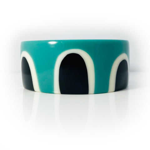Flat surfaced bracelet inlaid with a sixties inspired pattern. Cast in a combination of black, white and teal blue resin.