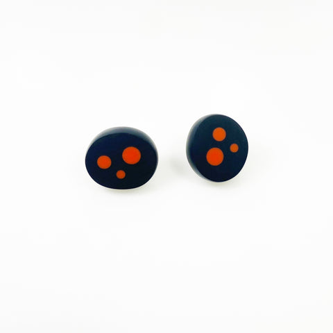 Oval shaped resin sud earrings cast in black and inlaid with orange polka dots. Fitted wit silver pins and disc plastic backs.