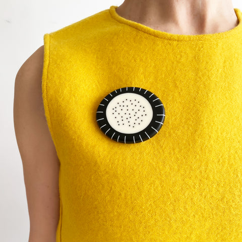 Large pebble shaped resin brooch cast in a black and white pattern of stripes and dots. Worn on bright yellow top.